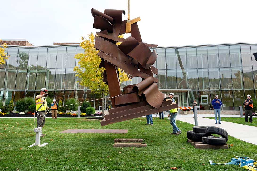 Large metal sculpture being lowered onto concrete pad