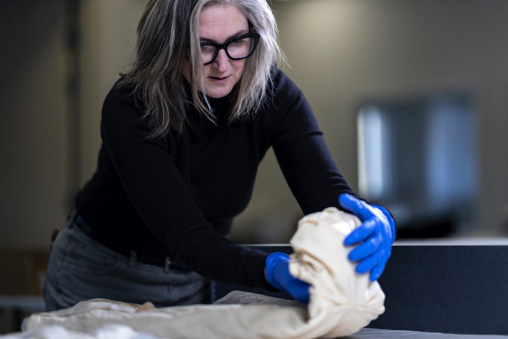 A woman wearing gloves carefully handles a dress