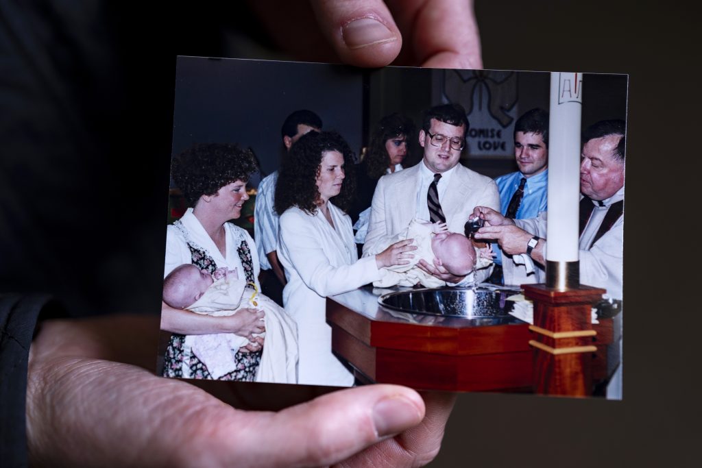 Hands hold a family photograph showing two babies getting baptized. 