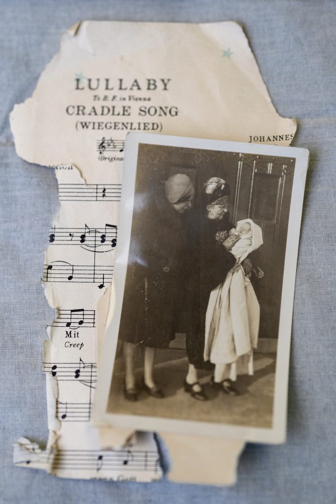 A vintage photograph of a baby wearing a long baptismal gown is juxtaposed with a ripped piece of sheet music. 