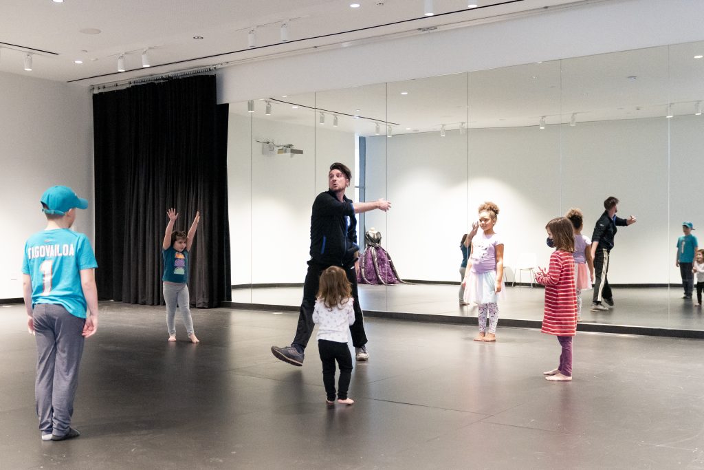 A person teaches a group of children how to dance in a studio.