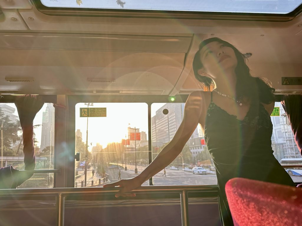 A woman inside a bus smiles and looks up.