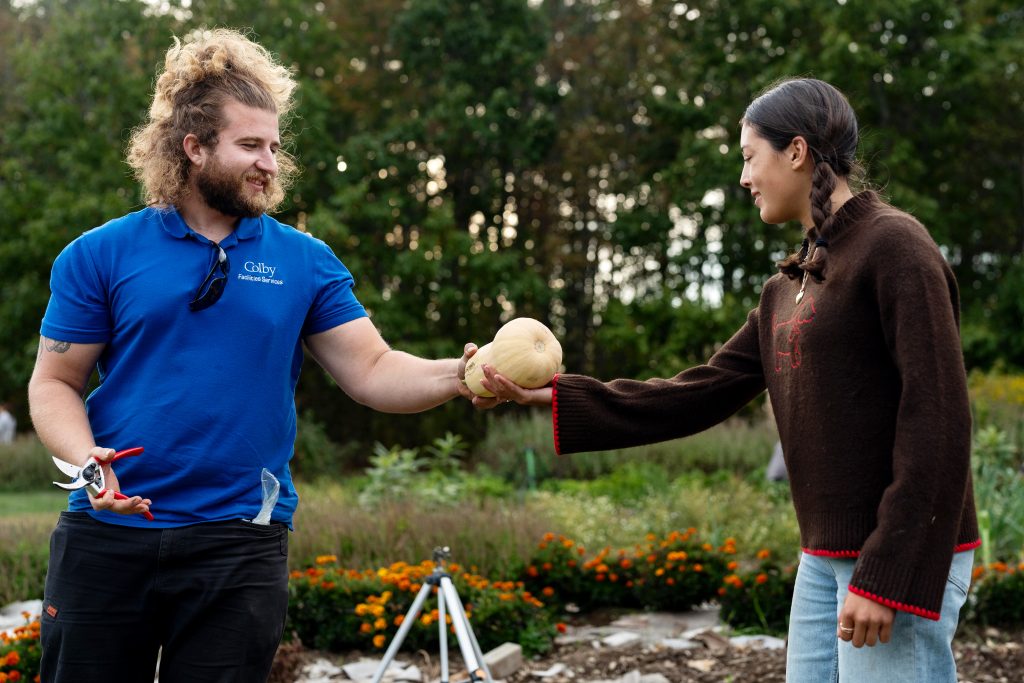 One person hands a butternut squash to a student at Colby's organic garden. 