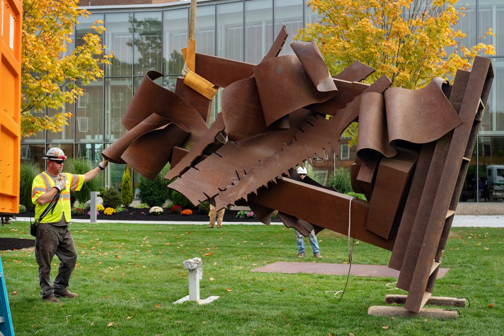 A worker holds the edge of a large metal sculpture while he talks on a radio.