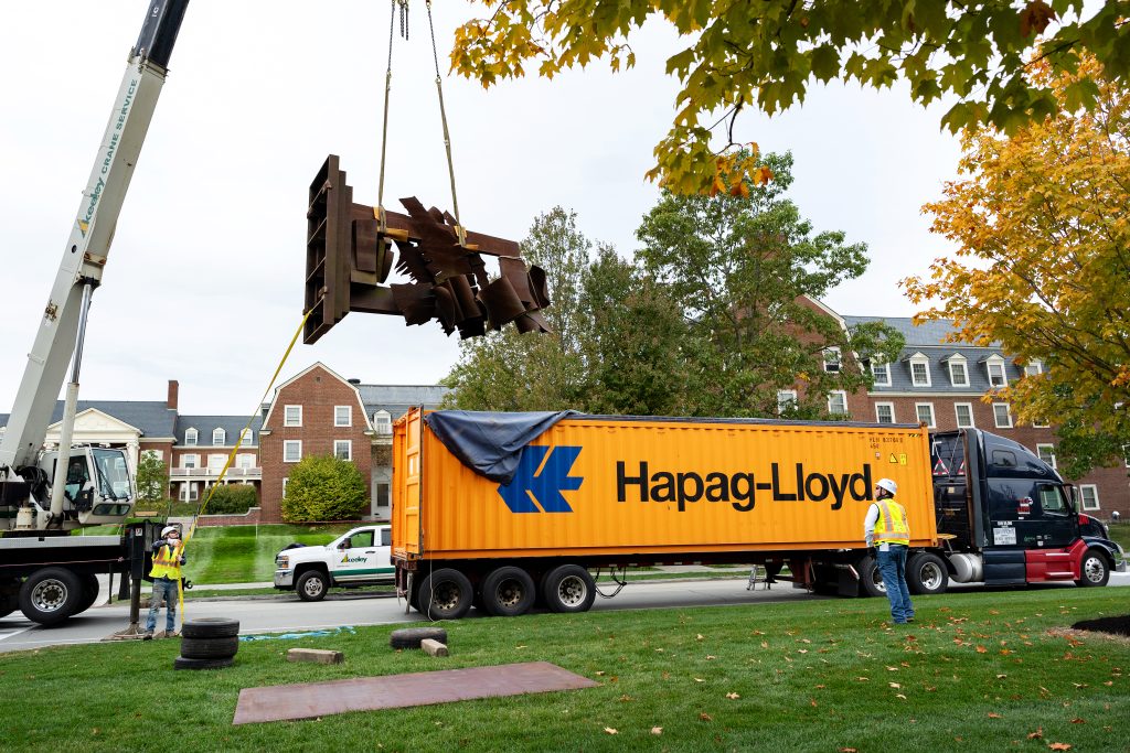 A metal art sculpture being raised from the back of a semi truck.