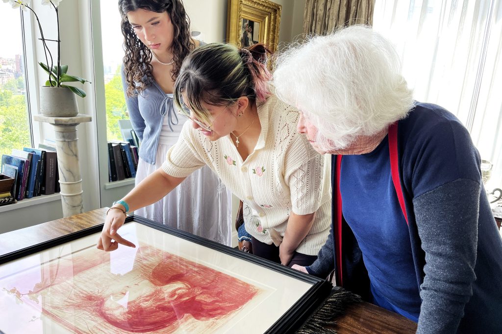 Three people examine a framed lithograph art piece.