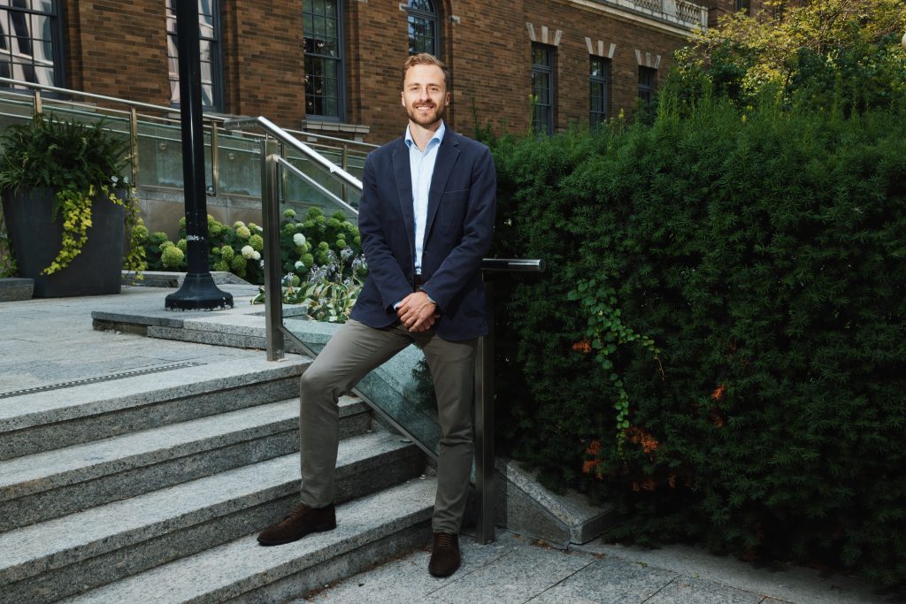Felix Baldauf-Lenschen '14, wearing a suit, poses outside a building. 