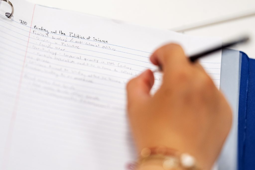 A hand with a pen, resting on a notebook.