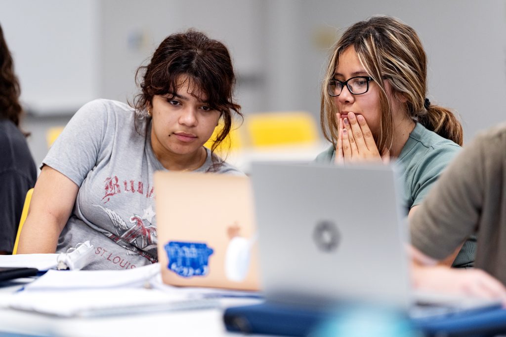 Two people sitting at a table looking at a laptop screen.