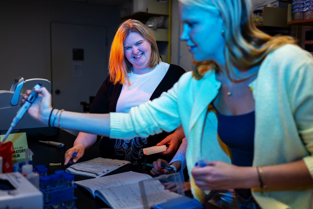 A student works on science research as a professor looks on attentively. 