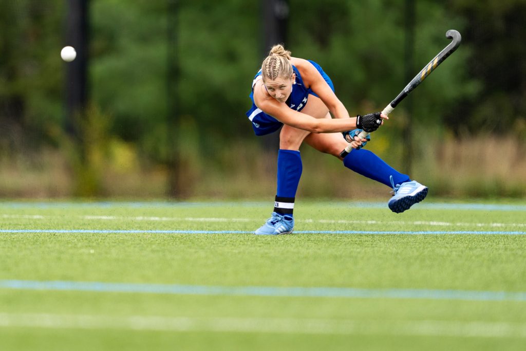 A field hockey player with arms swung to the side after hitting the ball.