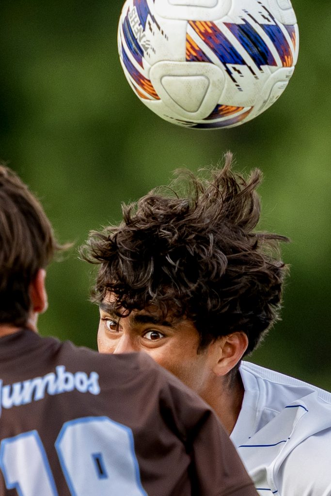 A soccer player heads the ball over his opponent.