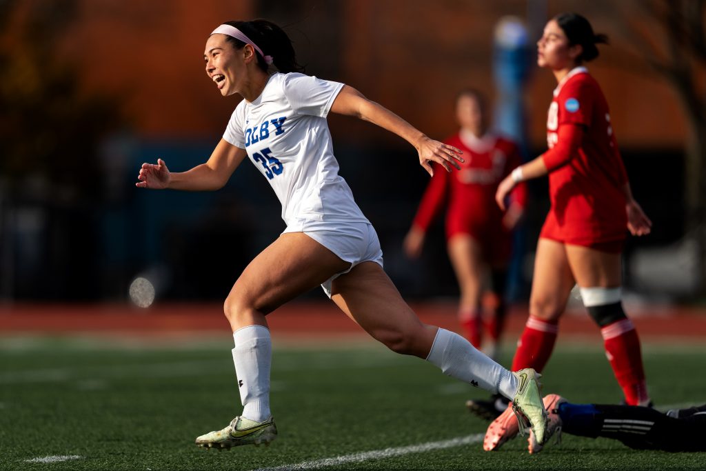 A soccer player runs past opponents to celebrate.