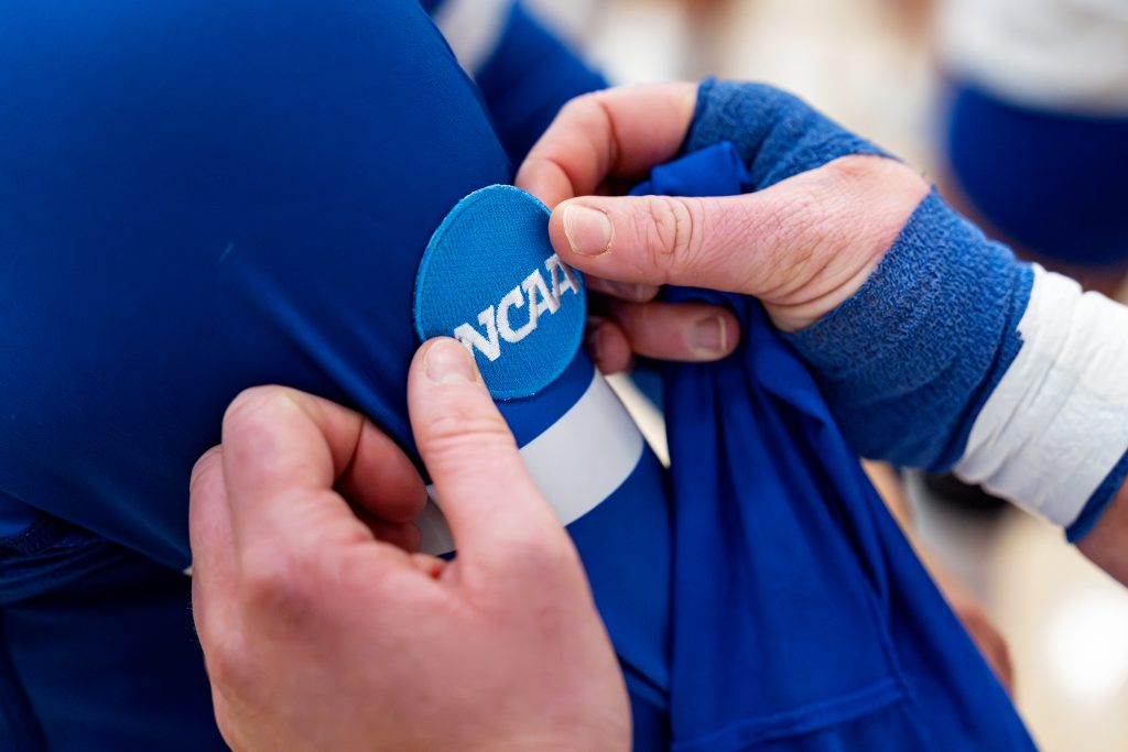 A circular patch with the letters NCAA being places on the sleeve of a volleyball player by another player.