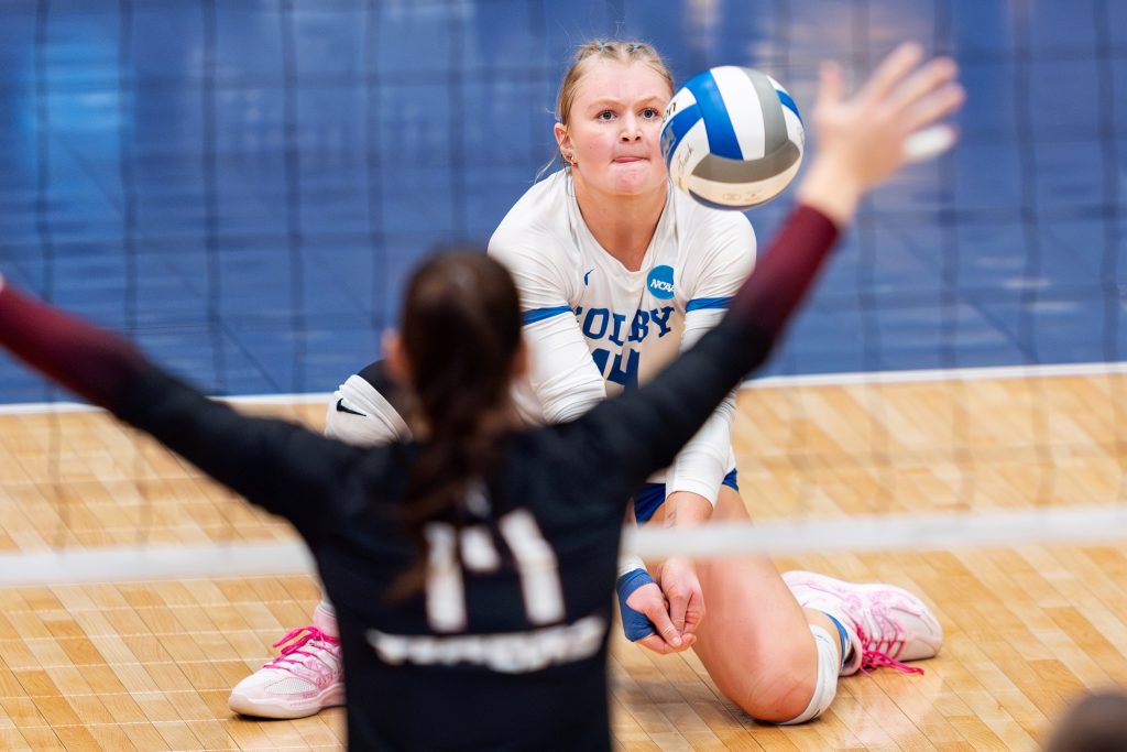 A volleyball player on one knee about to hit the ball over the net.