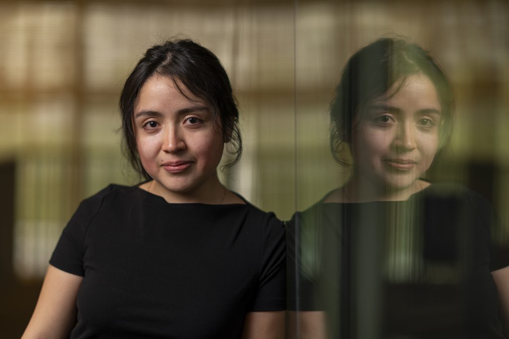 A woman standing next to reflective glass poses for a photo.