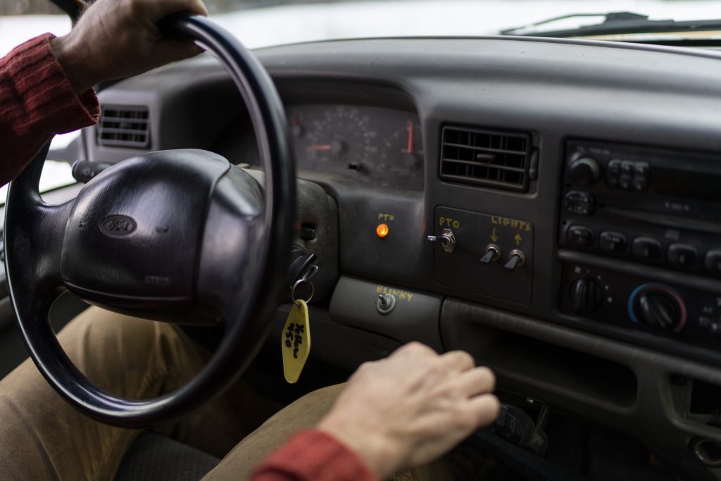 A person grips a steering with one hand as the other holds onto the stick shift.