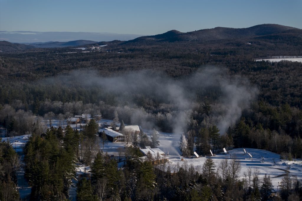 An aerial view of snow covered buildings amongst dense forest.