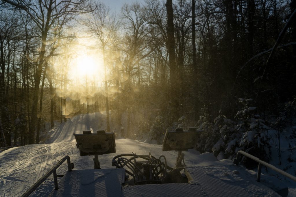 Sunrise illuminates the back of a snow groomer.