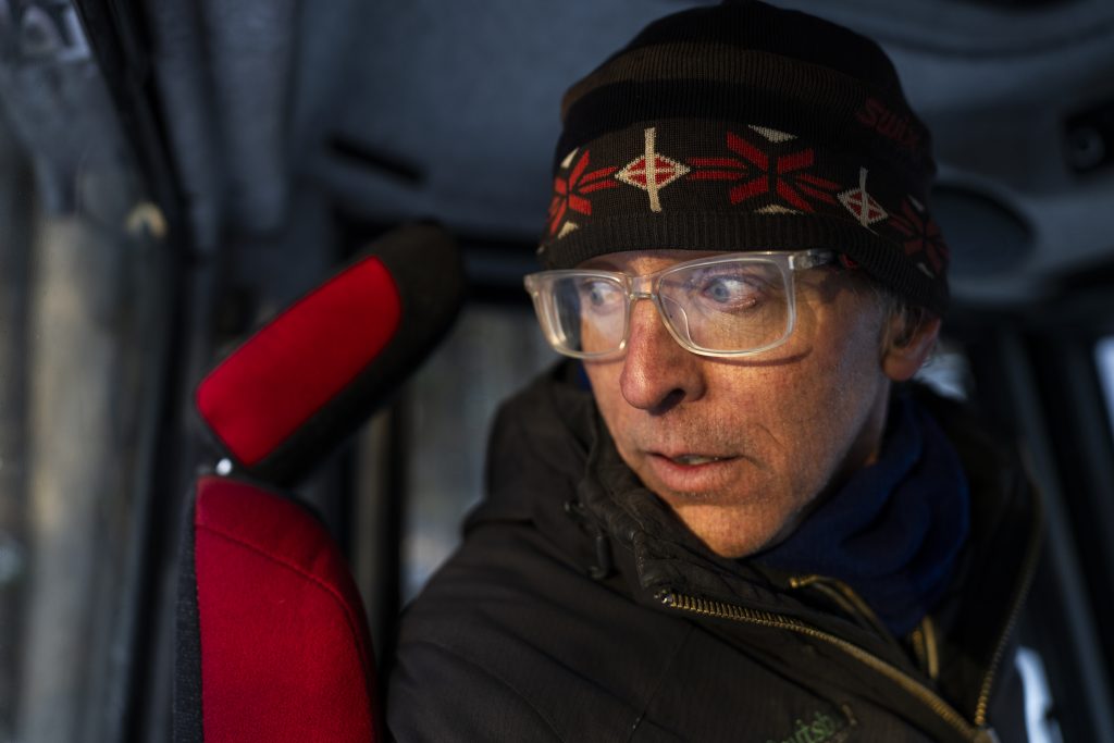 A man inside a truck cab with head turned looking out the rear window.