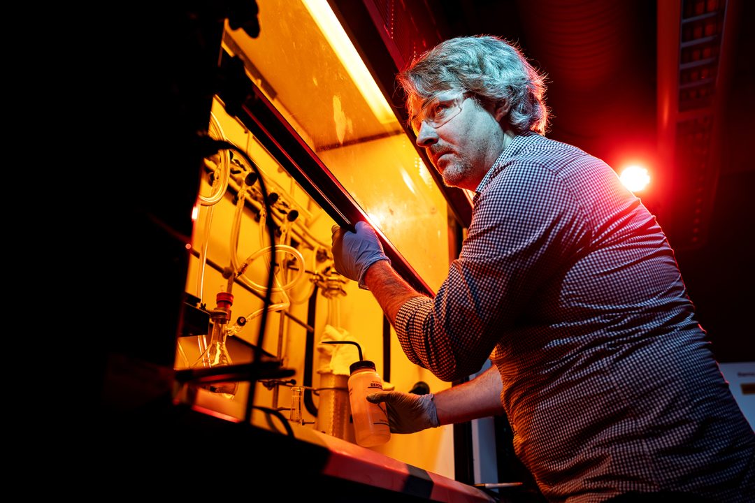 A man wearing safety goggles works in a science lab.