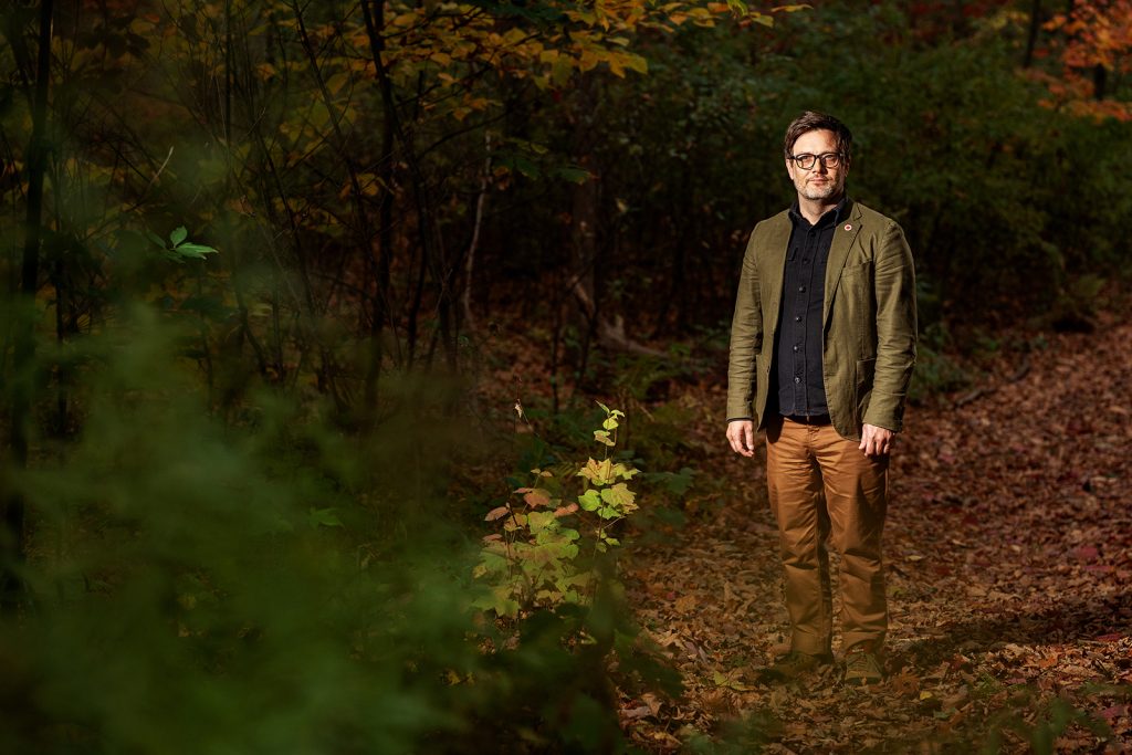 A man standing in a forest during autumn poses for a photo.