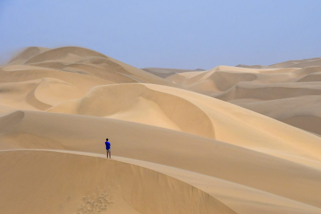An aerial view of a person standing on top of a sand dune in the desert.