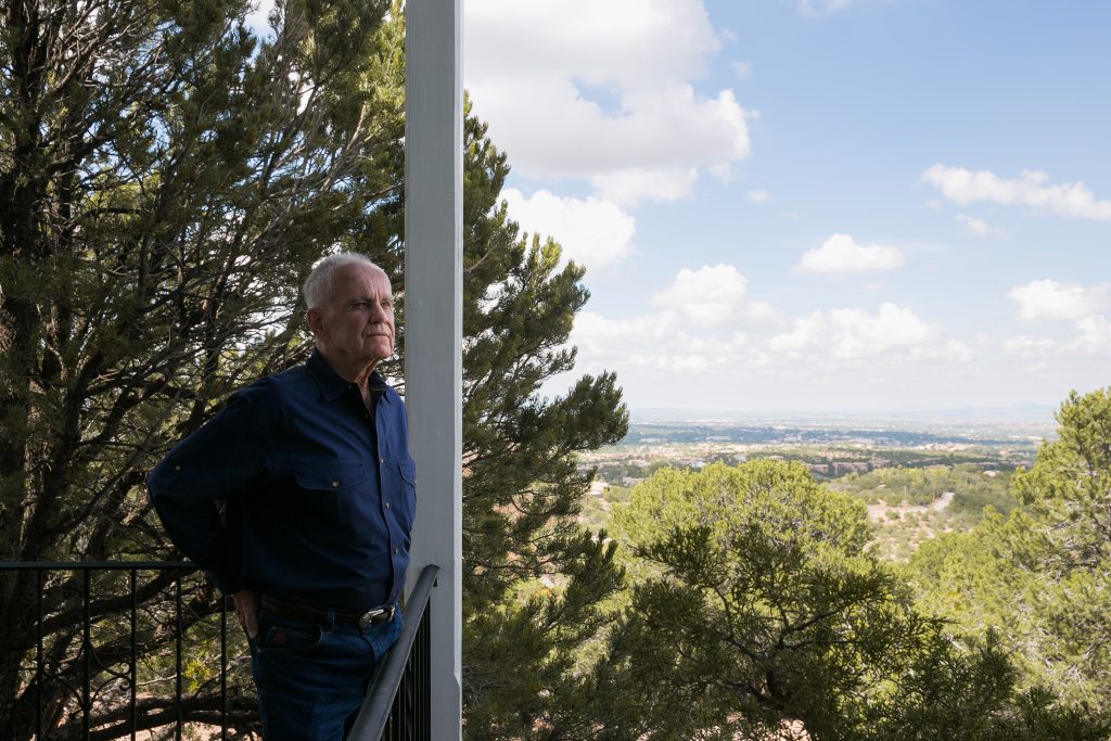 A man standing on a balcony overlooking foliage.