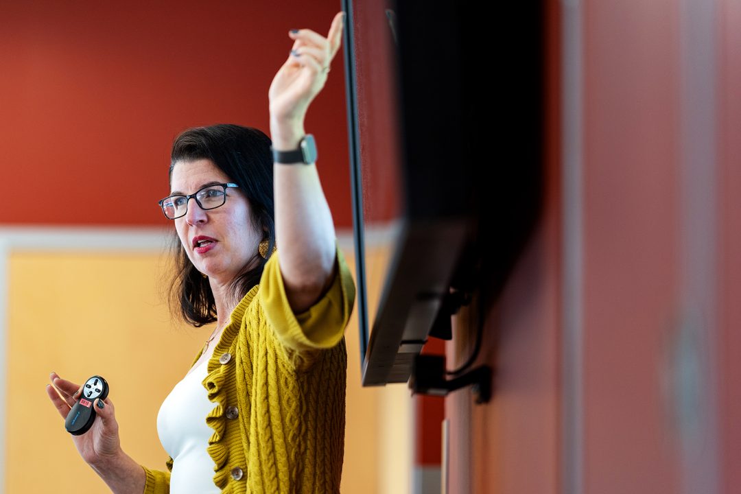 Adult woman point to a screen as she teaches a course