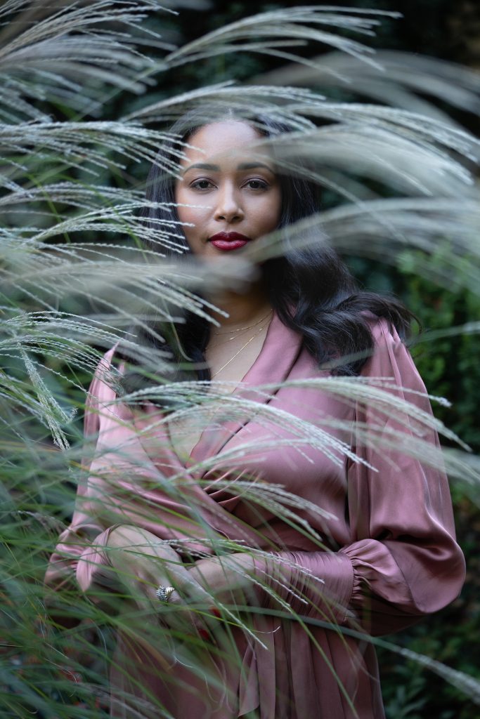 A woman wearing rose colored clothing standing between foliage.