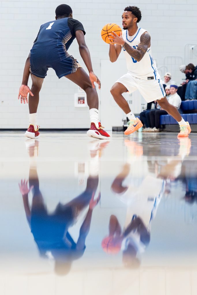 A basketball player advances forward with ball in hand as a defender stands in his way.