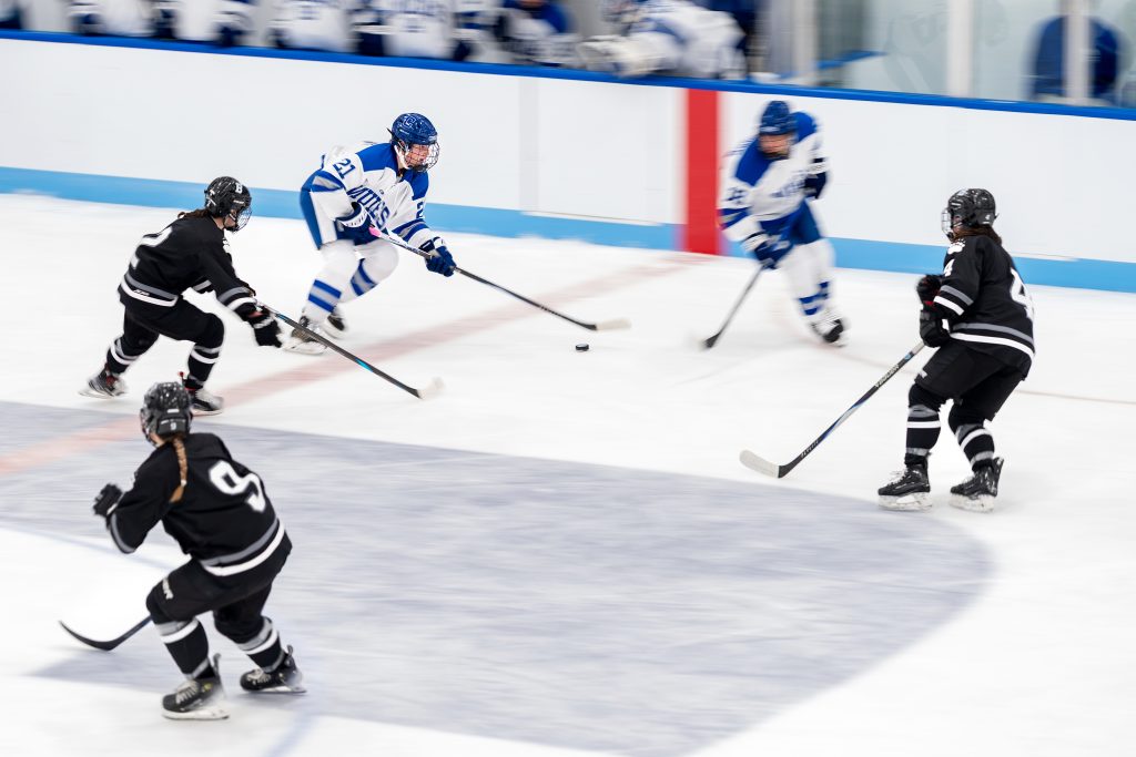 A hockey player moves the puck forward as three opponents defend.
