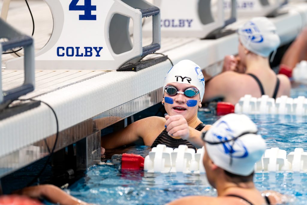 A Colby swimming athlete holds onto the edge of the indoor pool.