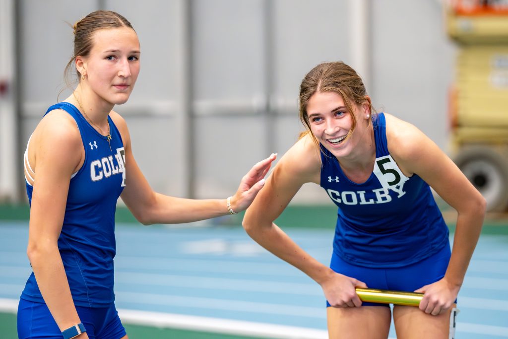 A relay runner doubled over in exhaustion as another rests a hand on her arm.