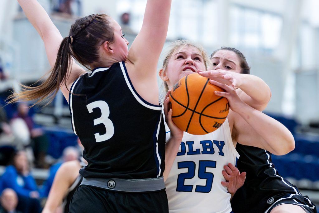 A Colby basketball player holding the ball while two rivals defend and block.