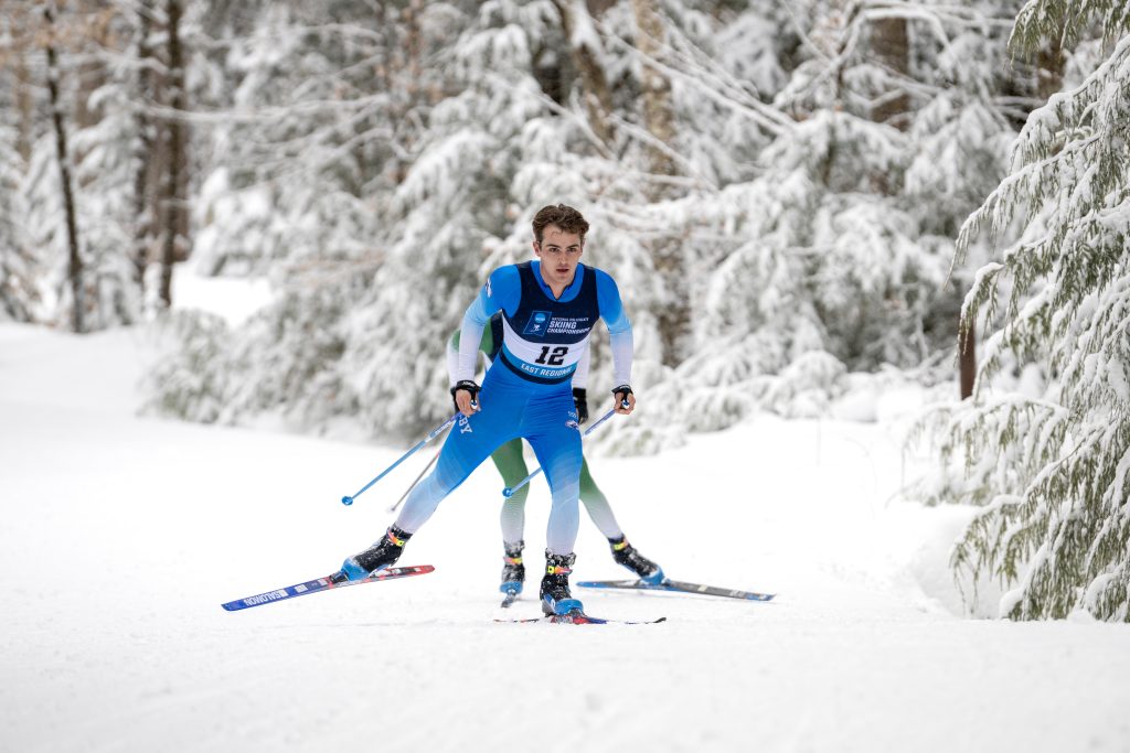 Two skiers, one behind the other on a flat trail.