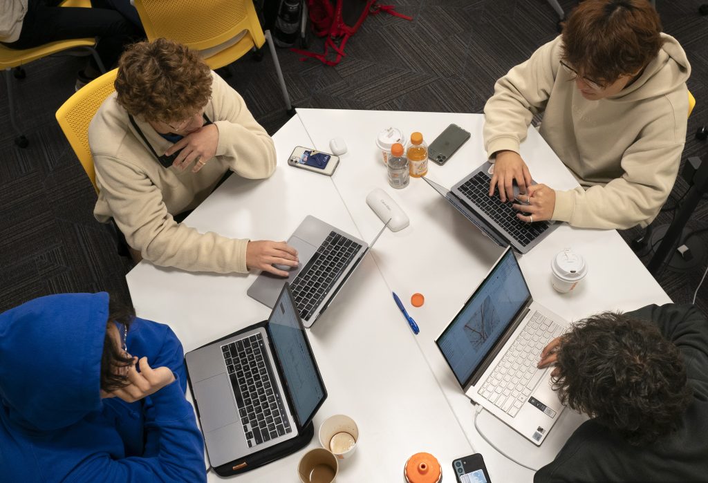 Students work at laptops set around a small table.