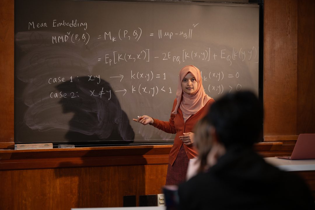 Female college professor wearing a hijab in front of a chalkboard