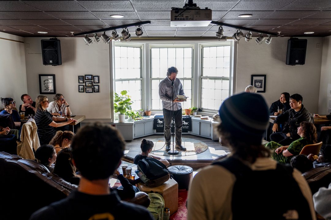 A poet in front of crowd in a coffeehouse for a reading