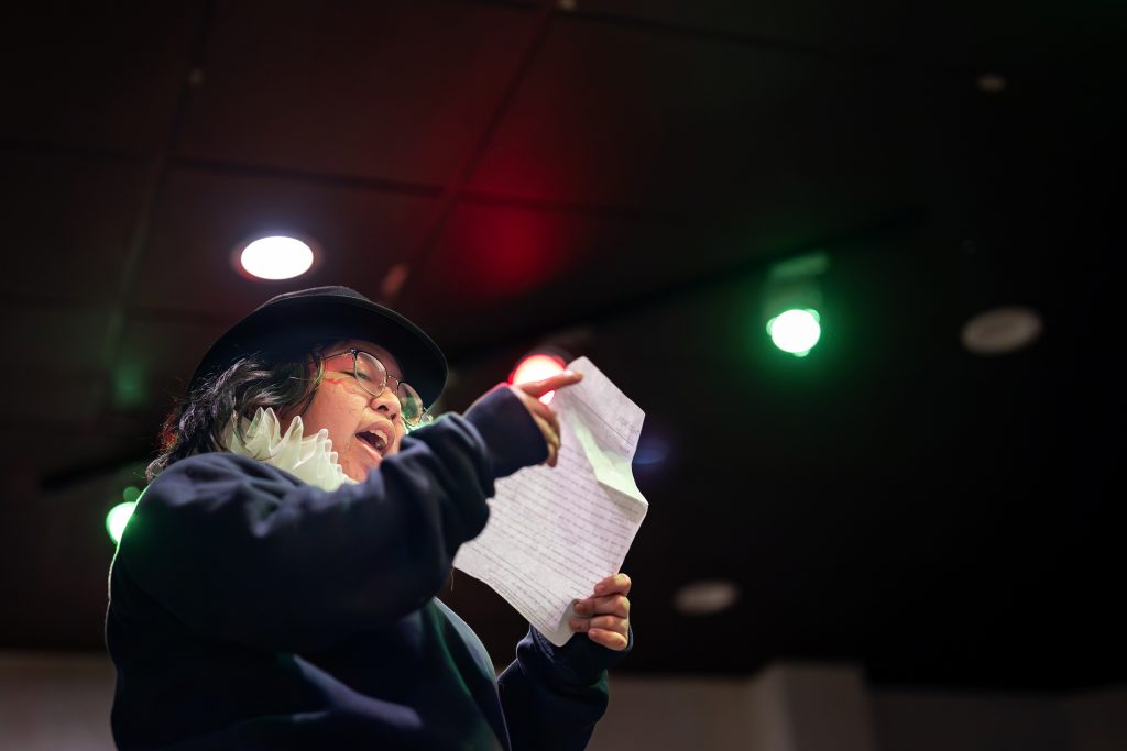 A student wearing a costume rehearses from a script.