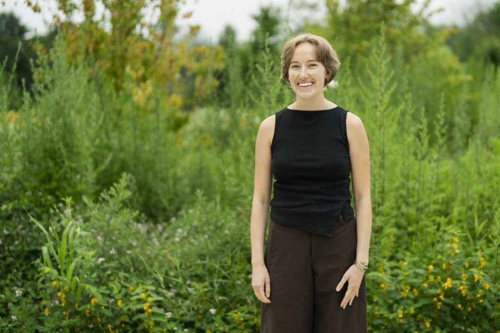 A woman smiles while standing in nature.