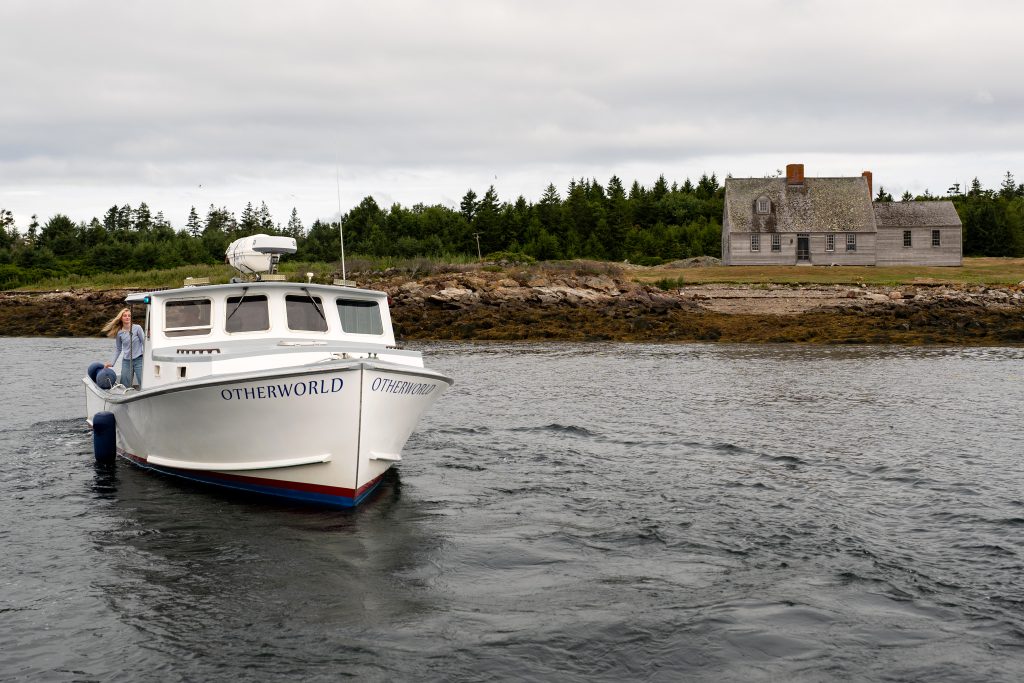 A person is on a boat with an island and a rustic house in the background. 