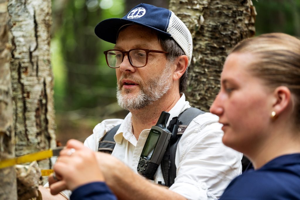 A professor helps a student measure a tree. 