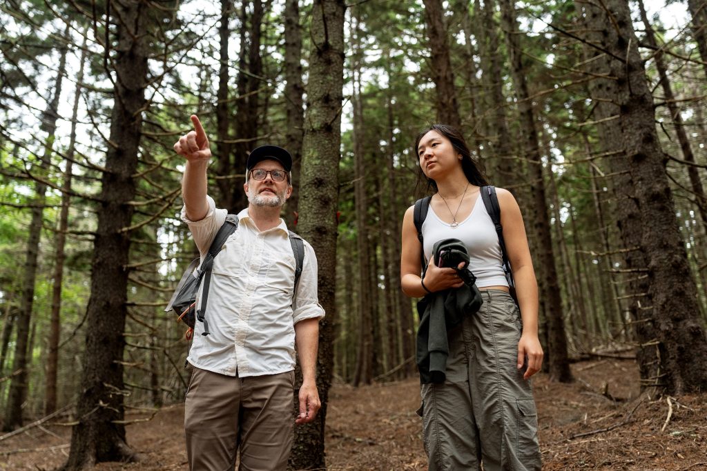 A professor and a student look at something in a forest.  
