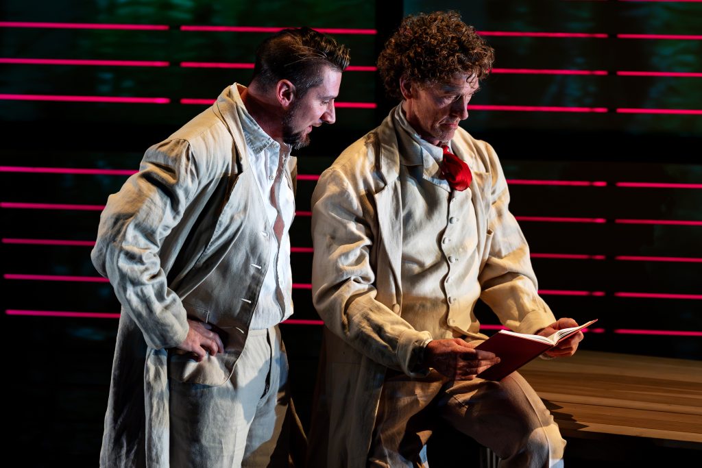 Two performers look at a book. 