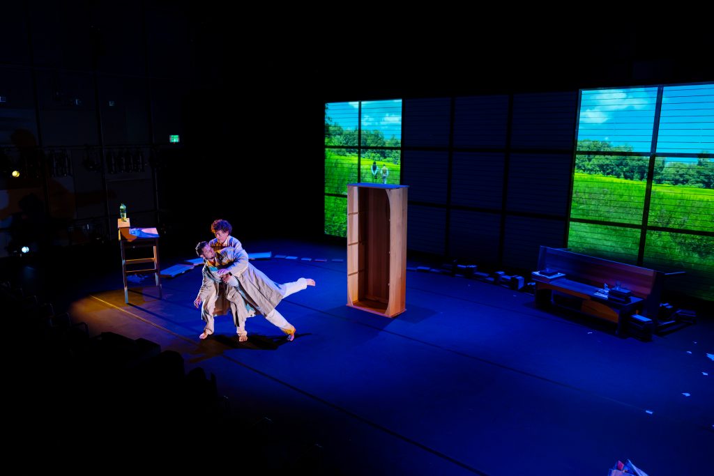 Two men dance on a dimly-lit stage. 